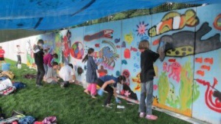 Kinder bringen die Bilder unter Anleitung eines professionellen Sprayers an die Wand